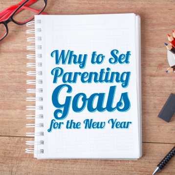 A spiral notebook with the text "Why to Set Parenting Goals for the New Year" on the cover, next to glasses and colored pencils on a wooden desk.