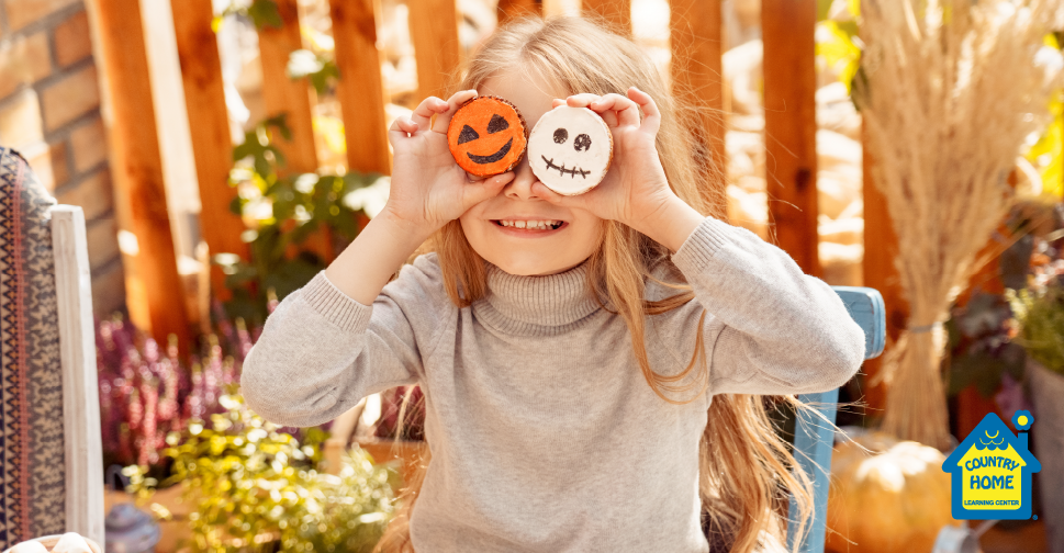 little girl in fall sweater holding halloween pumpkin and ghost cookies