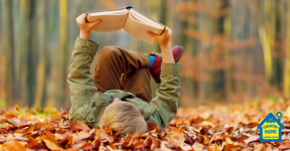 young boy reading a book in colorful fall leaves