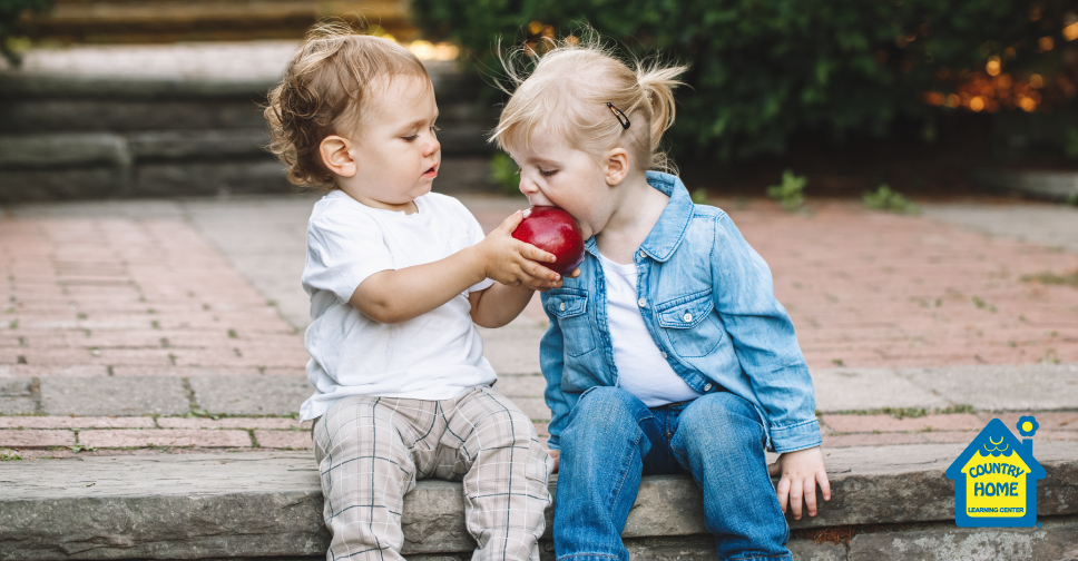 a toddler sharing his apple with another toddler