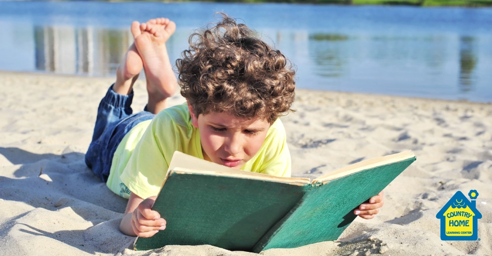 young boy reading a book on the beach