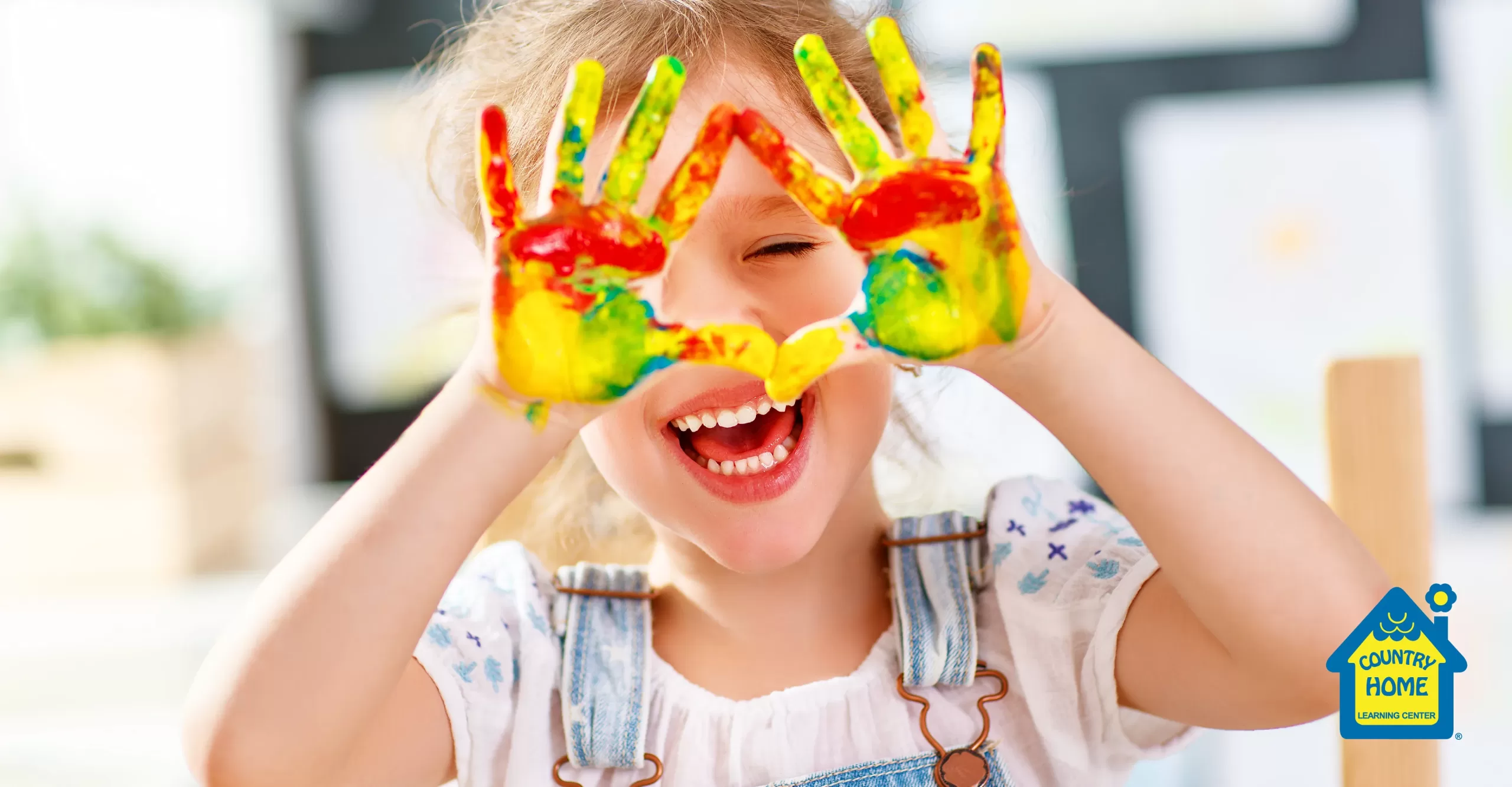 little girl golds up both hands covered in homemade finger paint while smiling.