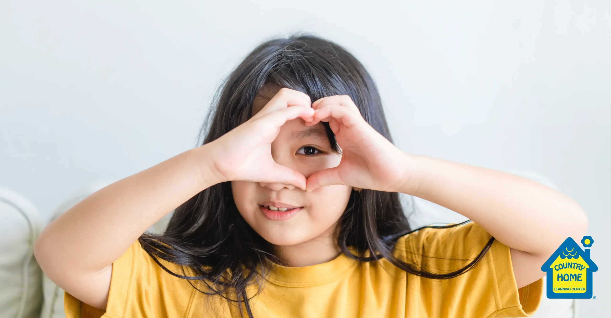 a little girl makes a heart shape around her eye with her hands