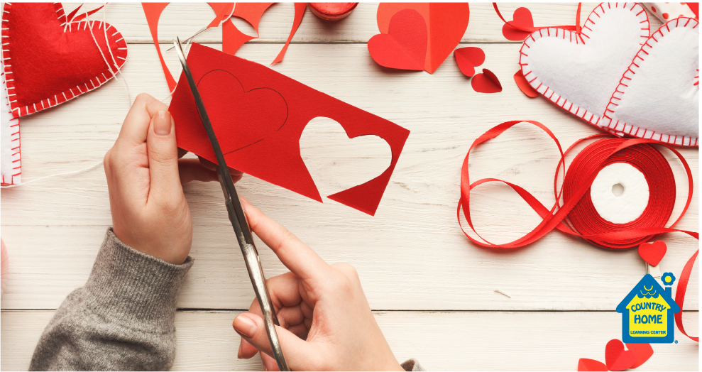 young child's hands cutting out a red paper heart