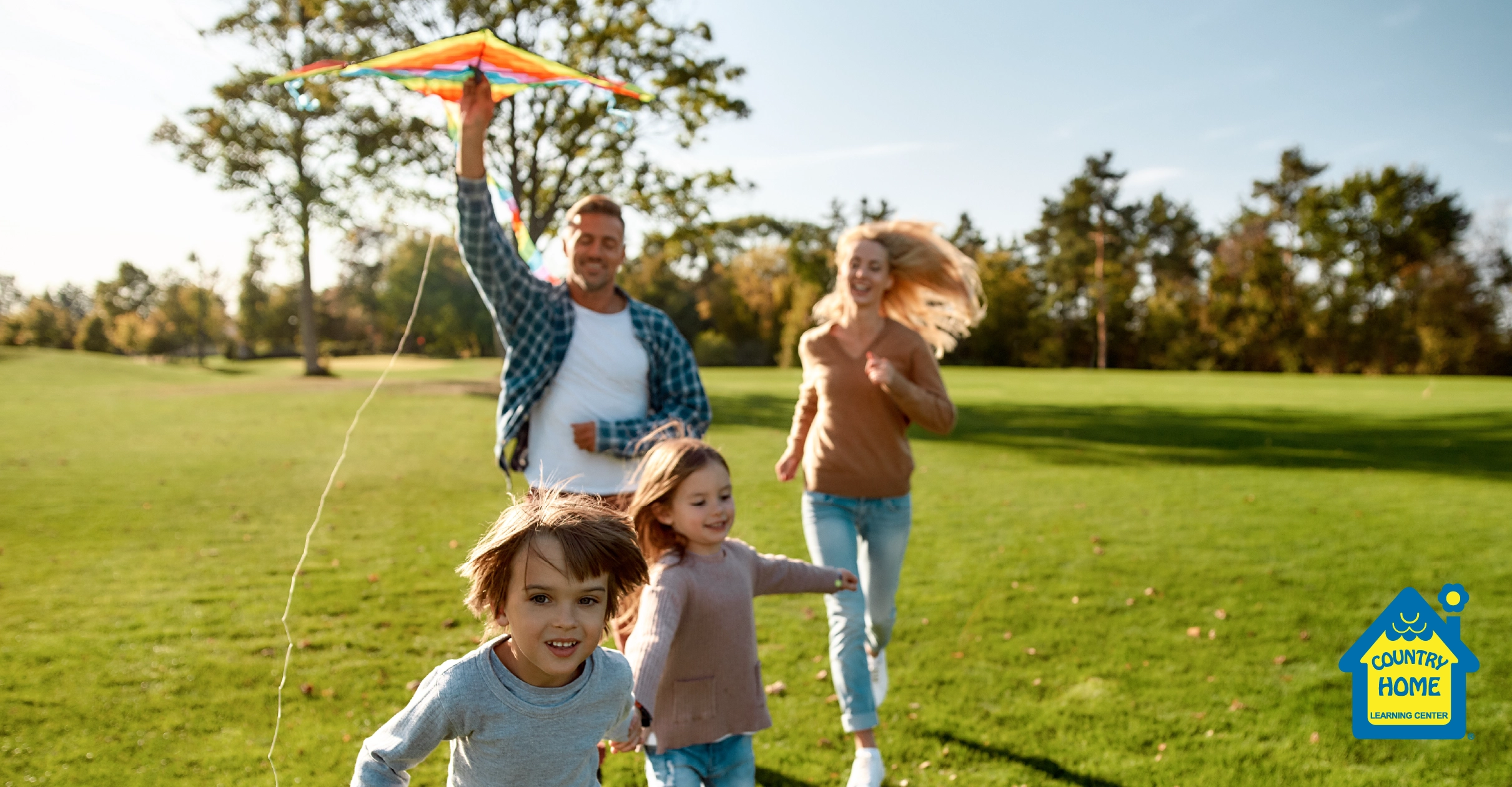 Family of four running around a park with a kite in hand