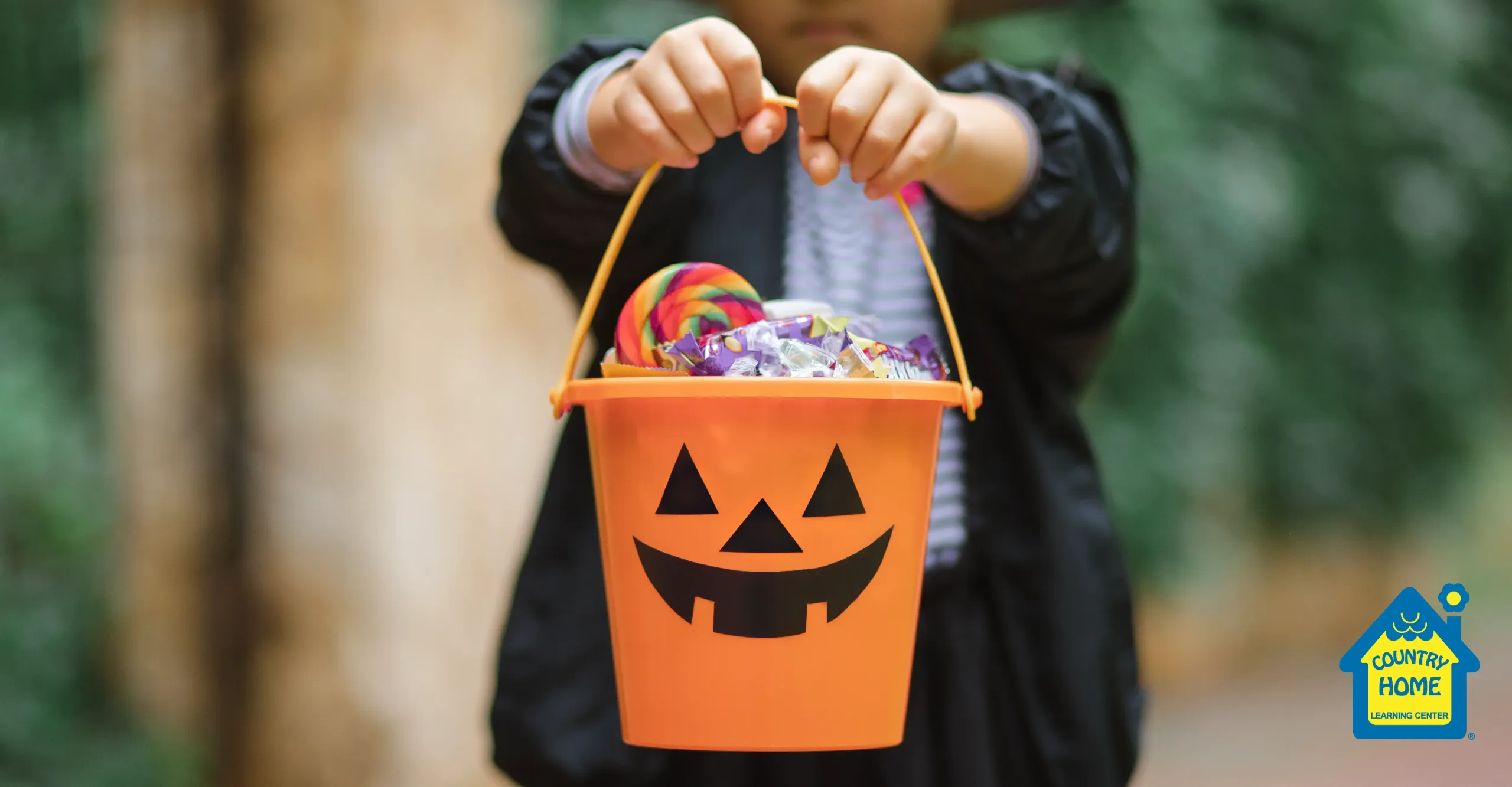 Child holding orange pumpkin candy bucket filled with colorful Halloween treats.