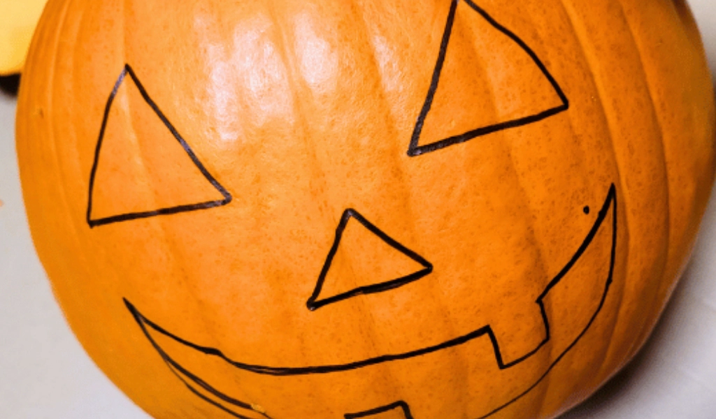 A pumpkin with a jack-o'-lantern face outlined in black marker, showing triangle eyes, a triangle nose, and a jagged mouth.