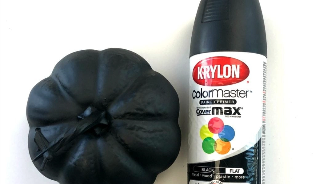A black-painted pumpkin sits next to a can of Krylon ColorMaster black spray paint.