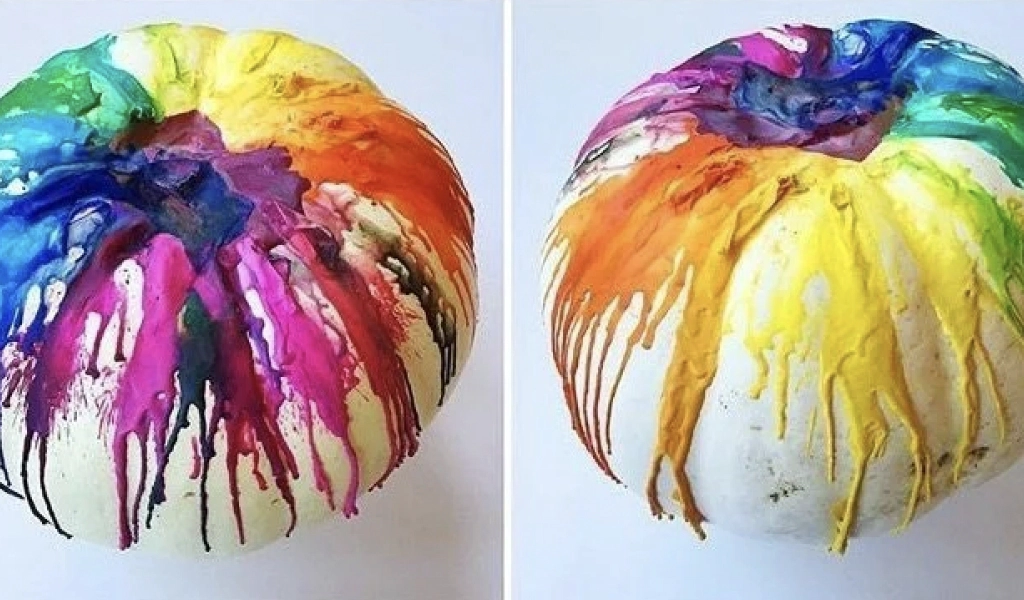 A white pumpkin with melted, multicolored wax dripped across the top and sides, creating a vibrant pattern.