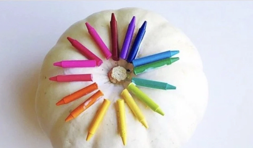 A white pumpkin with colorful crayon pieces arranged in a circular pattern on top.
