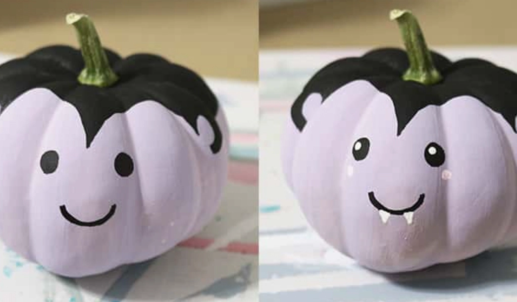 Two small pumpkins painted light purple with black tops, decorated with cartoon faces resembling vampires