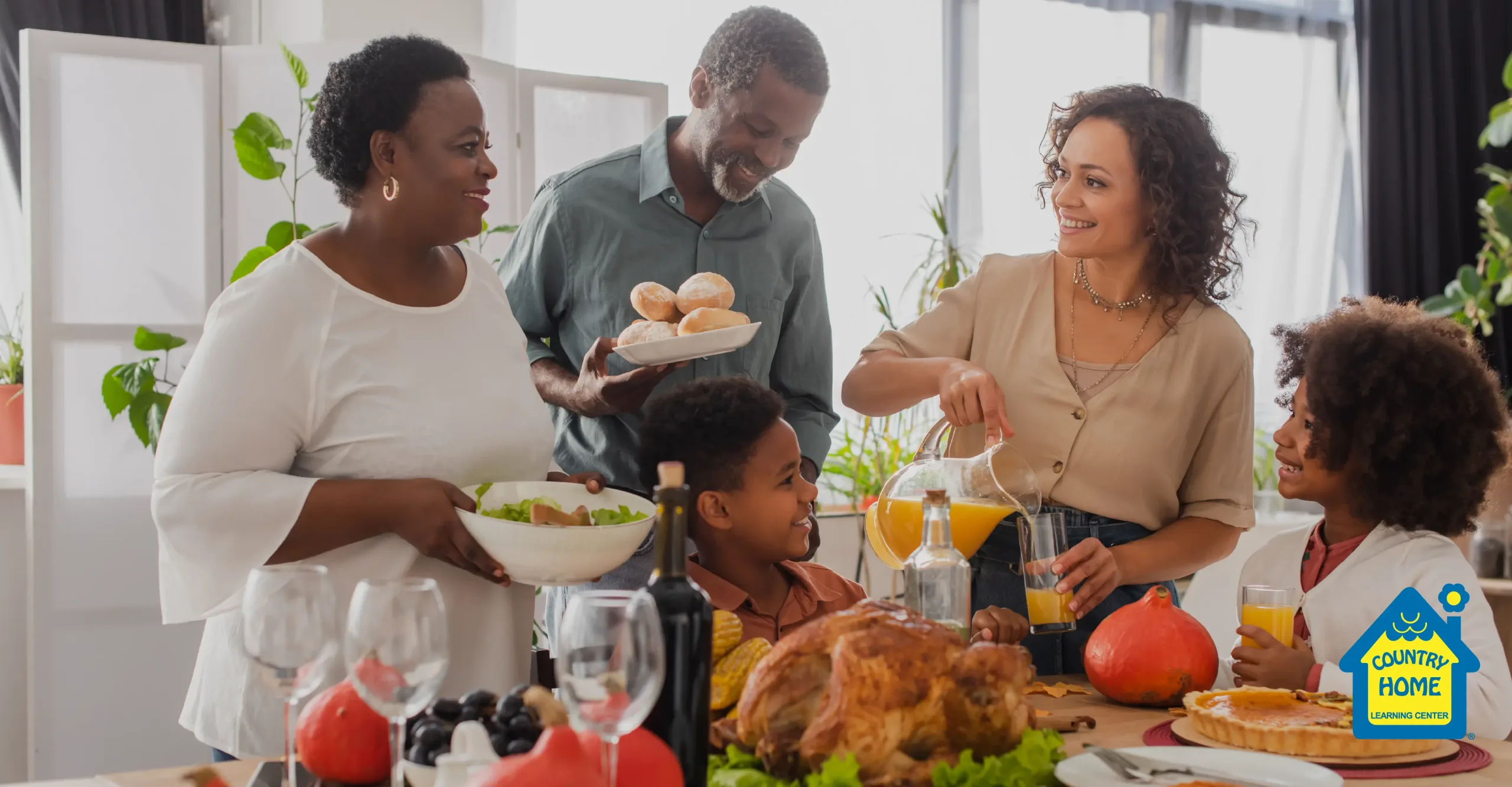 A family gathers around a table filled with Thanksgiving dishes, including roast turkey and fruit, as an adult pours orange juice for the children.