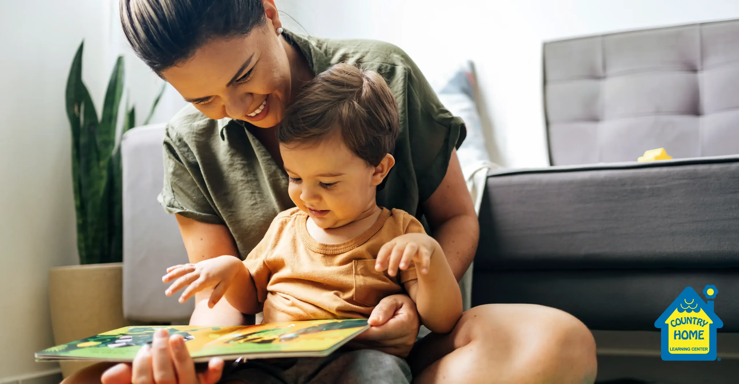 blog-630_How to Support Your Child’s Language Development in the New Year_rect An adult and a young child sit on the floor, smiling and looking at a picture book together, sharing a special early childhood moment. The "Country Home Learning Center" logo is visible in the bottom right corner.