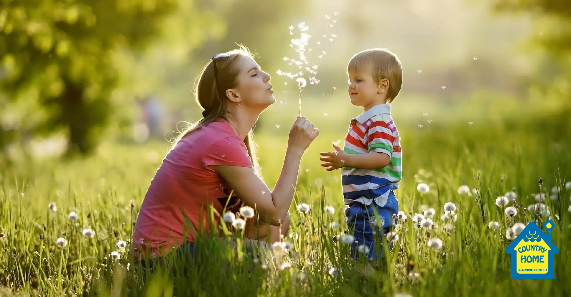 Mom and toddler playing outside blowing dandelions in a field.