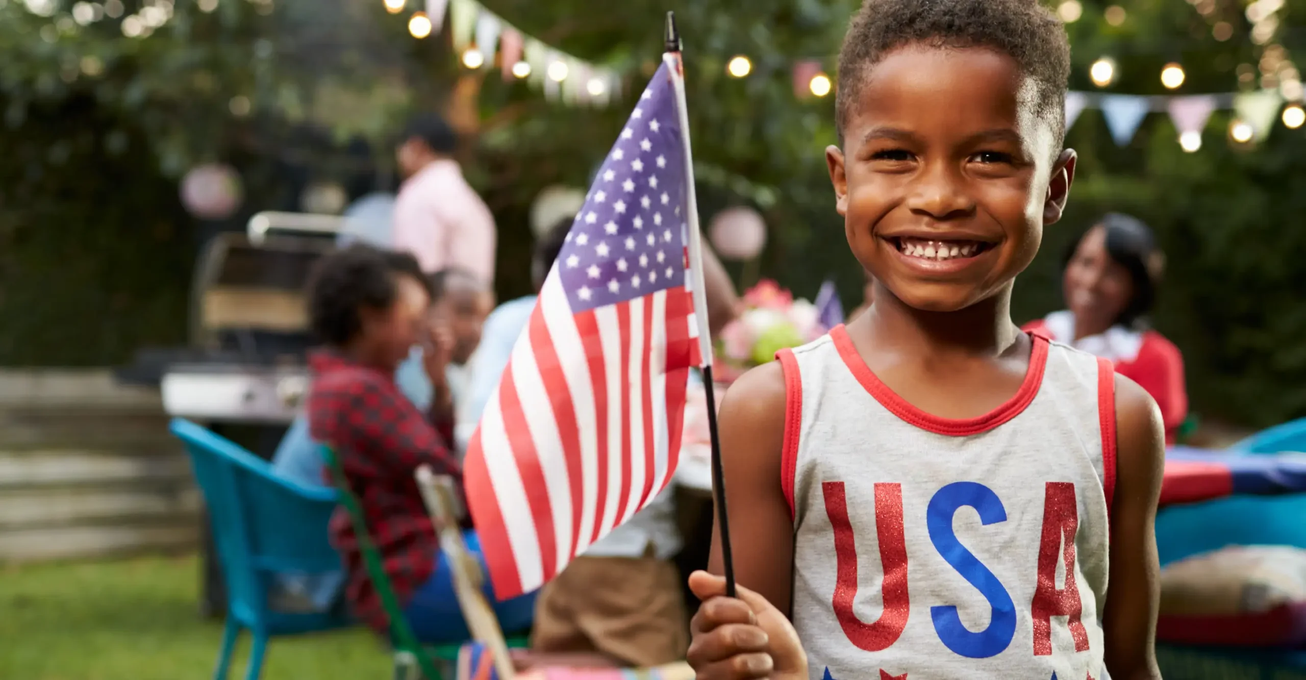 Boy waving American flag at Fourth of July picnic with family.